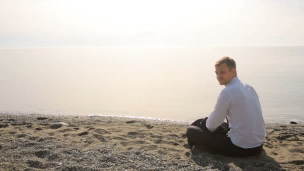 Бизнесмен в костюме, сидя на пляже жестом приглашает присоединиться к себе — стоковое видео