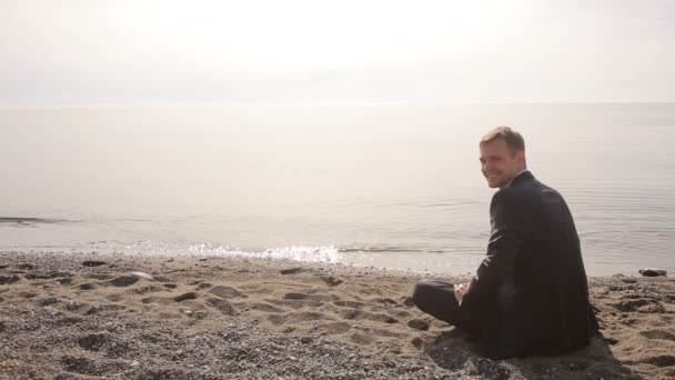Biznesmen w garnitur, siedząc na plaży gestem zaprasza do przyłączenia się do siebie — Wideo stockowe