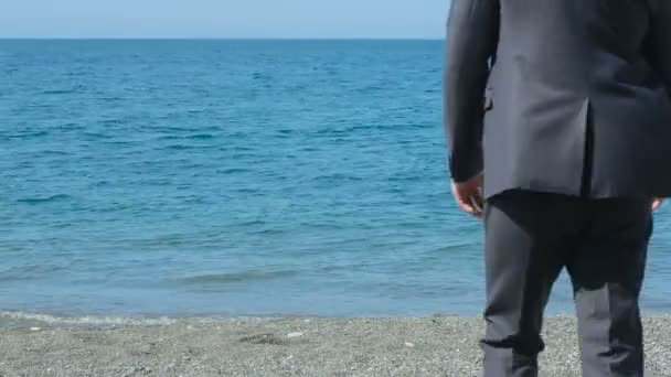 Affärsman promenader längs stranden i en kostym. beundrar den vackra stranden — Stockvideo
