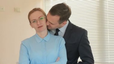 İki iş adamları erkek ve kadın ayakta ve gülümseyen, panjurlar ile penceresinin arka plan üzerinde Office ifadesiyle kameraya bakıyor. Onu öptü.