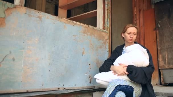 Utmattad kvinna, mor med ett spädbarn i famnen på bakgrunden av bombade hus. Krig, jordbävning, brand — Stockvideo