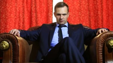 Zalim bir adam mağrurca kameraya bakan bir deri koltukta oturan bir takım,