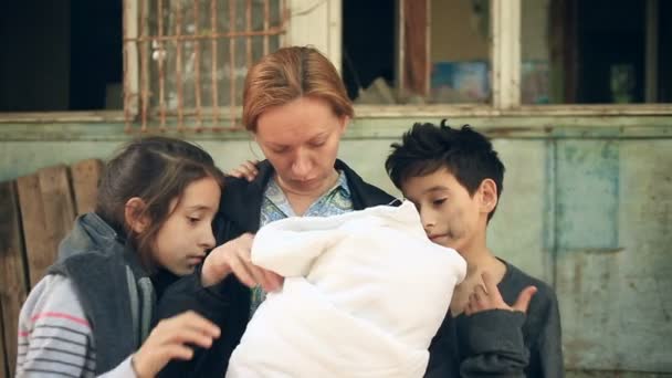 Niños refugiados y su madre con un niño en brazos en el fondo de casas bombardeadas. Guerra, terremoto, fuego — Vídeos de Stock