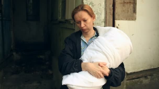 Donna esausta, madre con un bambino tra le braccia sullo sfondo di case bombardate. Guerra, terremoto, fuoco — Video Stock