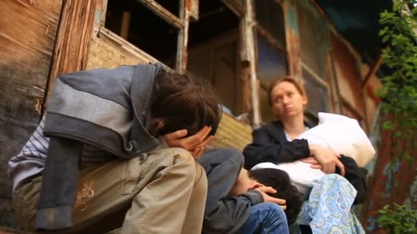 Niños refugiados y su madre con un niño en brazos en el fondo de casas bombardeadas. Guerra, terremoto, fuego — Vídeos de Stock