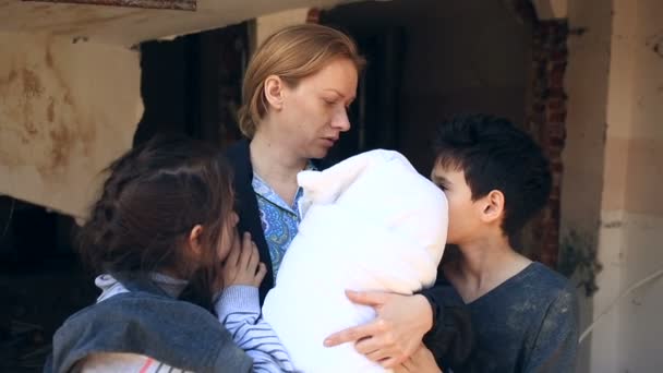 Refugee children and their mother with a child in their arms amid destroyed houses. War, earthquake, fire, bombing — Stock Video