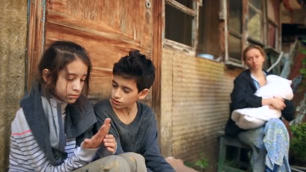 Crianças refugiadas e sua mãe com uma criança em seus braços em meio a casas destruídas. Guerra, terremoto, fogo, bombardeio — Vídeo de Stock