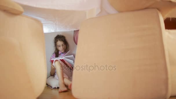 Een meisje zit in een geïmproviseerde huis kussens en een deken-huis — Stockvideo