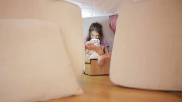 Une petite fille est assise dans une maison de fortune d'oreillers et une maison de couverture — Video