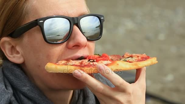 Žena sedí o samotě na opuštěné pláži za špatného počasí, se dívá na moře a žere pizzu — Stock video