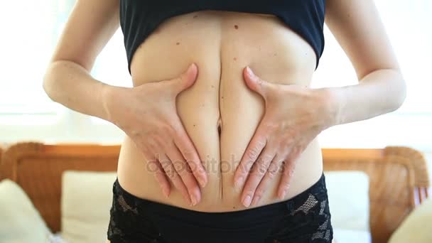 A woman is a fat stomach. Overweight and weight loss concept. A girl in a bathing suit pulls the skin on her stomach, which is stretched and flabby after losing weight or giving birth to a baby — Stock Video