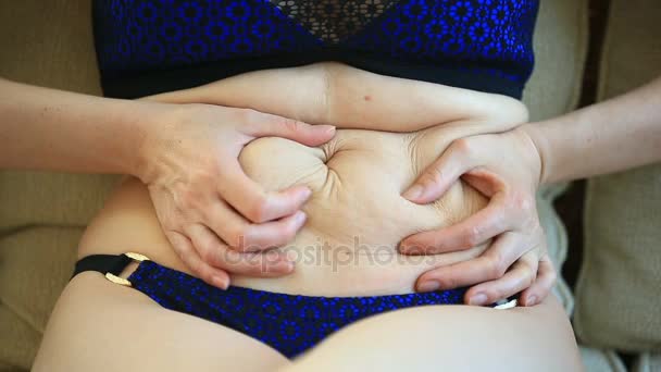 A woman is a fat stomach. Overweight and weight loss concept. A girl in a bathing suit pulls the skin on her stomach, which is stretched and flabby after losing weight or giving birth to a baby — Stock Video