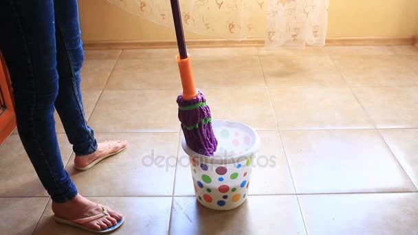En kvinna tvättar golvet i köket med en mopp. Doppa en trasa i en färgglad hink — Stockvideo