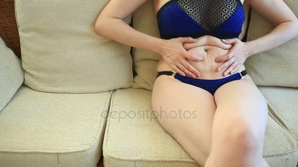 Žena je tuku žaludek. Nadváha a hubnutí koncept. Dívka v plavkách táhne kůži na břiše, který je roztažený a ochablá po ztrátě hmotnosti nebo porodu na dítě — Stock video