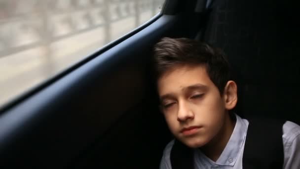 Niño adolescente cabalga en coche mirando por la ventana. Fuera de la ventana brillaron los árboles y las casas de la ciudad — Vídeos de Stock