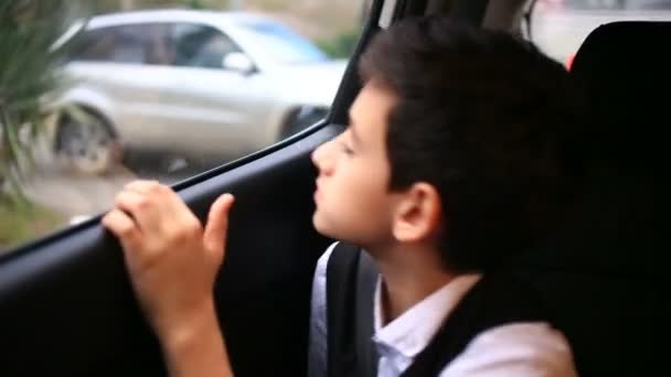 Niño adolescente cabalga en coche mirando por la ventana. Fuera de la ventana brillaron los árboles y las casas de la ciudad — Vídeos de Stock