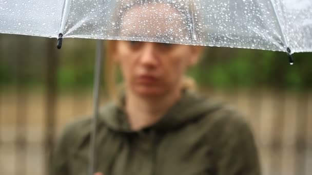 Разочарованный погодой, стоит под зонтиком во время дождя. Несчастная женщина — стоковое видео
