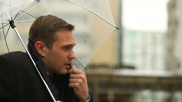 Розчарований погодою, що стоїть під парасолькою під час дощу. Нещасливий чоловік у костюмі — стокове відео