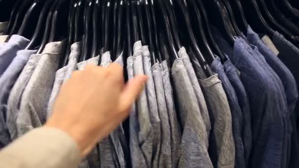 Мужчина выбирает одежду для себя в магазине одежды — стоковое видео
