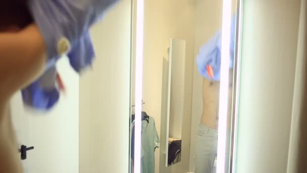 En man väljer kläder för sig själv i en klädaffär. Försöker på nya kläder i provrum — Stockvideo