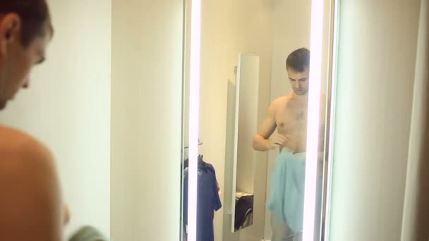 Een man kiest kleding voor zichzelf in een kledingwinkel. Proberen op nieuwe kleding in de paskamer — Stockvideo