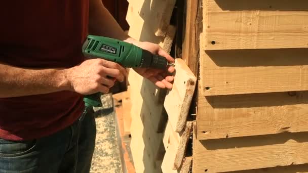 Primer plano, las manos carpintero clavan el tablero contra una pared de madera con un martillo y clavos — Vídeo de stock