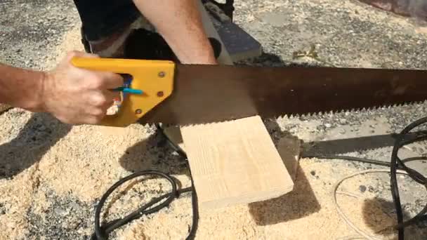 Um homem a serrar tábua de madeira com serra manual. Fechar. . — Vídeo de Stock