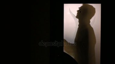 Bir cam kapının arkasında bir adam silüeti. İş elbisesi değişiyor.