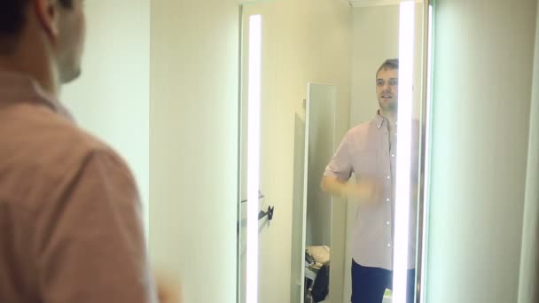 En man väljer kläder för sig själv i en klädaffär. Försöker på nya kläder i provrum — Stockvideo