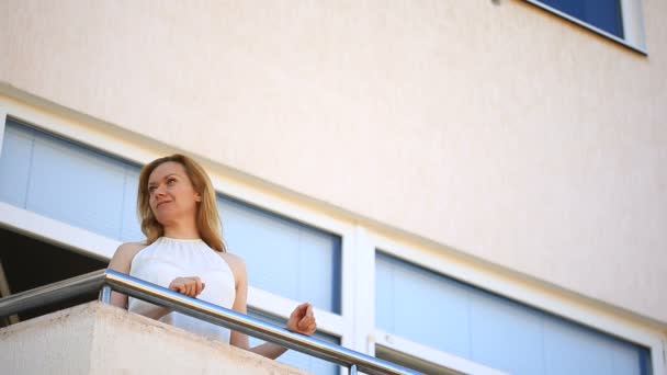 Mladá žena vystoupí na balkon a rozhlíží. Ona se usmívá a hledí do dálky — Stock video