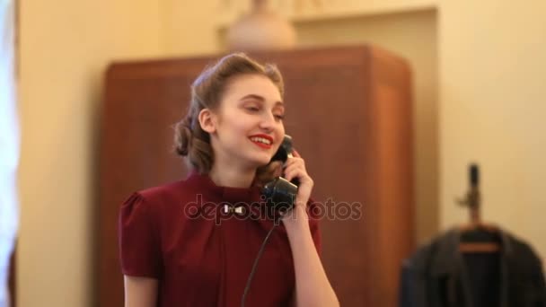 Happy pin-up girl in a retro style dress. Girl with positive emotions. Model poses for a photographer next to a rare telephone set — Stock Video