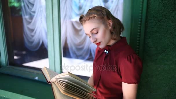 Ευτυχισμένο το pin-up κορίτσι σε ένα φόρεμα στυλ ρετρό. Κορίτσι με θετικά συναισθήματα. Μοντέλο θέτει για μια φωτογραφία πυροβολούν σε στυλ ρετρό. Αυτή διαβάζοντας ένα βιβλίο στο μπαλκόνι — Αρχείο Βίντεο