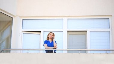 Genç bir kadın balkona adımlar ve etrafına bakıyor. O gülümsüyor ve mesafe içine dik dik bakıyor. Evet