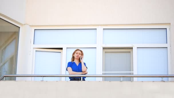 Mladá žena vystoupí na balkon a rozhlíží. Ona se usmívá a hledí do dálky. Mluvil po telefonu — Stock video