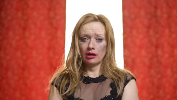 Beautiful sad woman with red lipstick and makeup cries on a red against white background. Makeup and mascara are smeared over the face — Stock Video