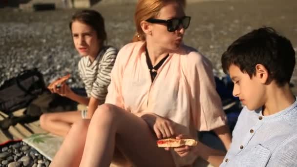 Gyermekek anyja pizzát eszik a strandon — Stock videók