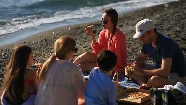 Přátelé s dětmi jíst pizzu na pláži. Piknik u moře na pláži — Stock video