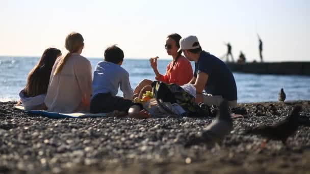 Vänner med barn som äter pizza på stranden. Picknick vid havet på stranden — Stockvideo