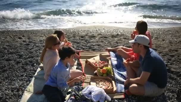 Amigos con niños comiendo pizza en la playa. Picnic junto al mar en la playa — Vídeos de Stock