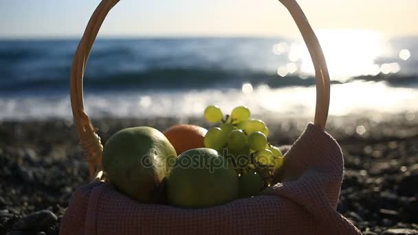 Cesta de frutas en la playa. La mano toma las uvas del racimo de uvas contra el fondo de las olas del mar — Vídeos de Stock