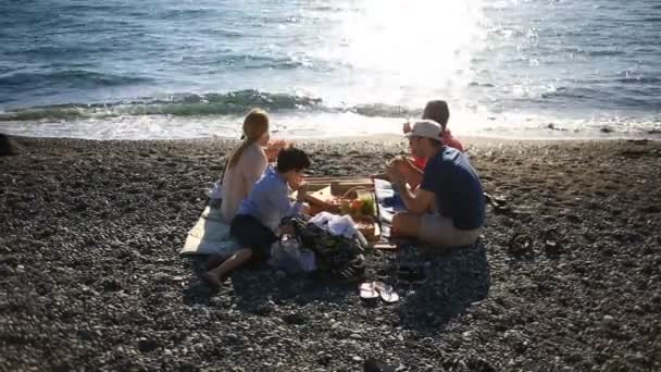 Vrienden met kinderen eten pizza op het strand. Picknick aan de zee op het strand — Stockvideo