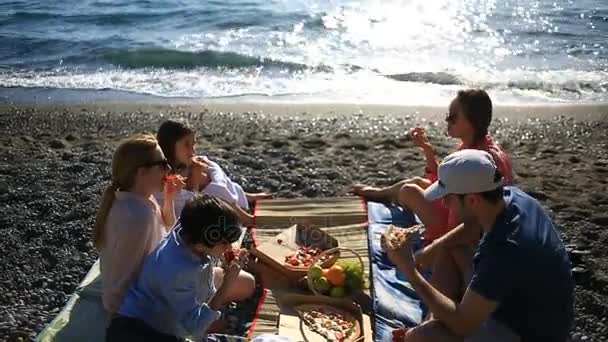 Amigos con niños comiendo pizza en la playa. Picnic junto al mar en la playa — Vídeo de stock