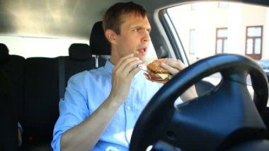 Bir araba direksiyon başında otururken hızlı yemek yeme iş adamı. Hamburger