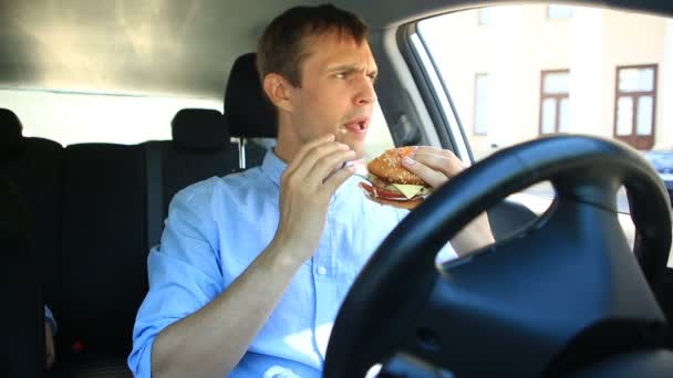 Biznesmen, jedzenie fast food, siedząc za kierownicą samochodu. Hamburger — Wideo stockowe