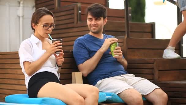 Un par de chicos y una chica están tomando café y charlando en un café informal al aire libre. Comida rápida — Vídeos de Stock