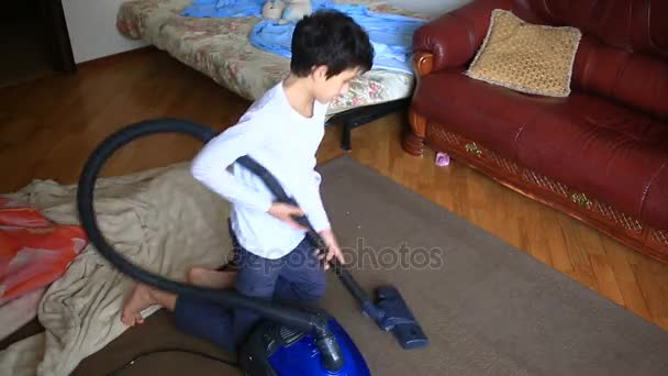Pojken rengör mattan i rummet med en dammsugare — Stockvideo