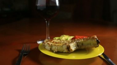 Pirzola kemikleri üzerinde Close-Up bir ızgarada pişirilir. Izgara et ızgara sebze ile bir tepside yatıyor. Yakınlarda bir kadeh kırmızı şarap olduğunu