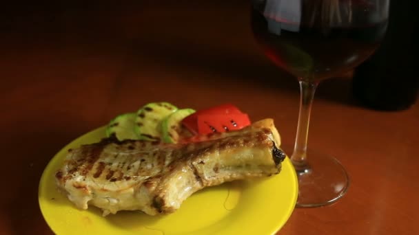 Close-up van schnitzels op botten gekookt op een grill. Gegrild vlees ligt op een schotel met gegrilde groenten. In de buurt is een glas rode wijn — Stockvideo