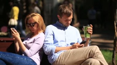 Erkek ve kadın bir bankta oturan farklı yönlere bakıyor. Herkes onun cep telefonu bakıyor