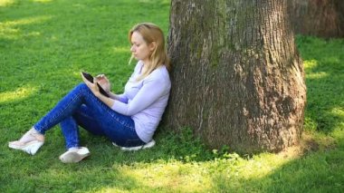Bir palmiye ağacının altında oturan ve browsing belgili tanımlık enterne üstünde bir smartphone yakışıklı kadın